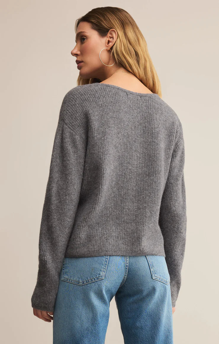 Woman wearing a gray sweater and blue jeans on a beige background