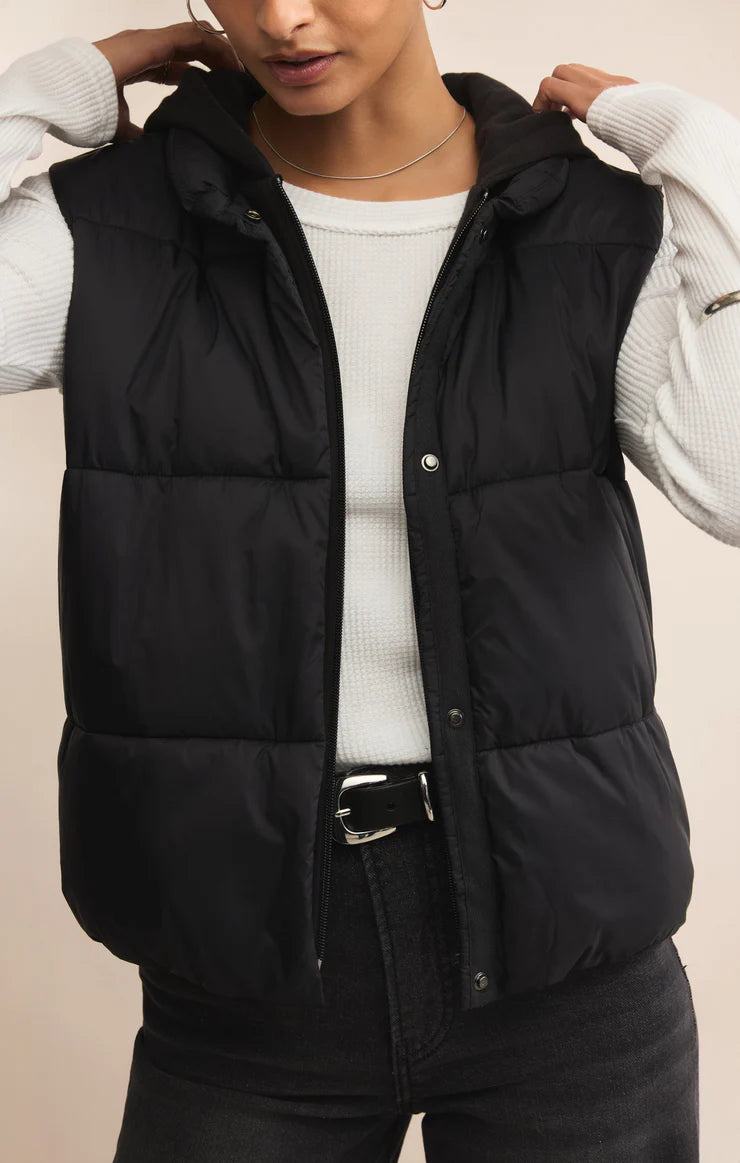 Person wearing a black puffer vest over a white sweater on a beige background
