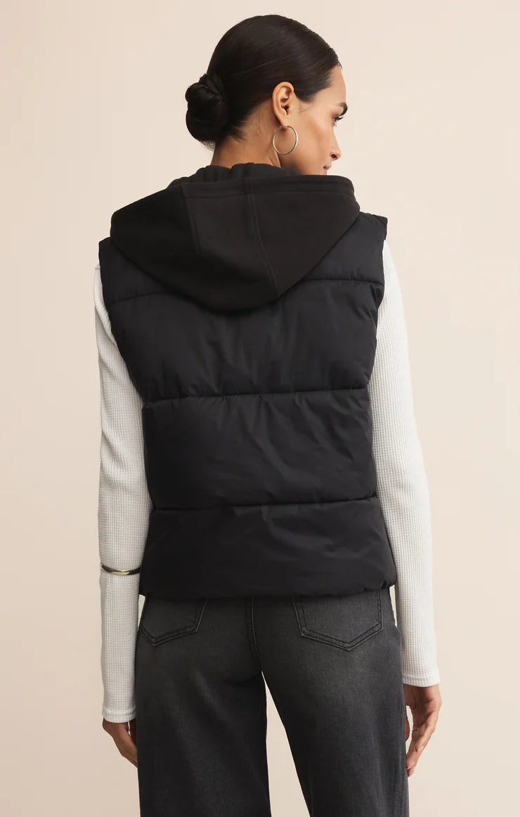 Person wearing a black puffer vest over a light-colored shirt on a beige background