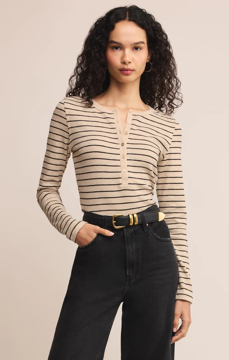 Woman wearing a striped long-sleeve Henley half button top and black pants on a beige background