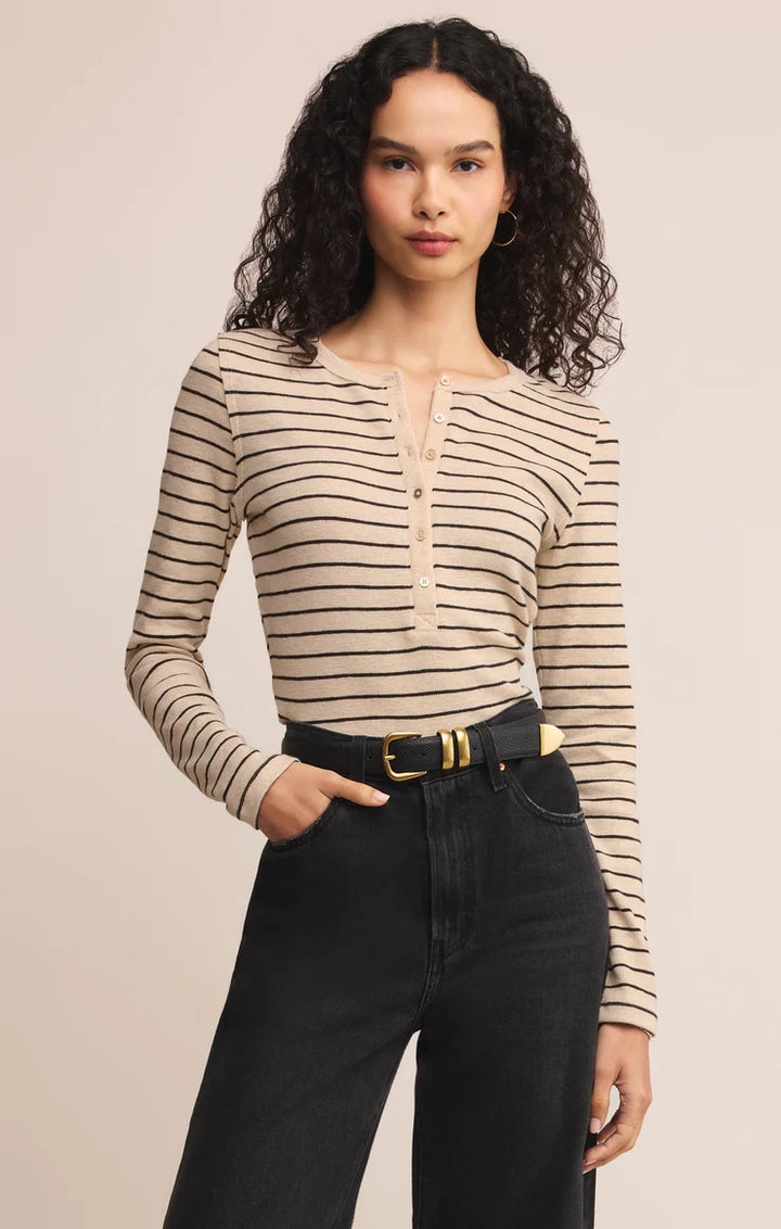 Woman wearing a striped long-sleeve Henley half button top and black pants on a beige background