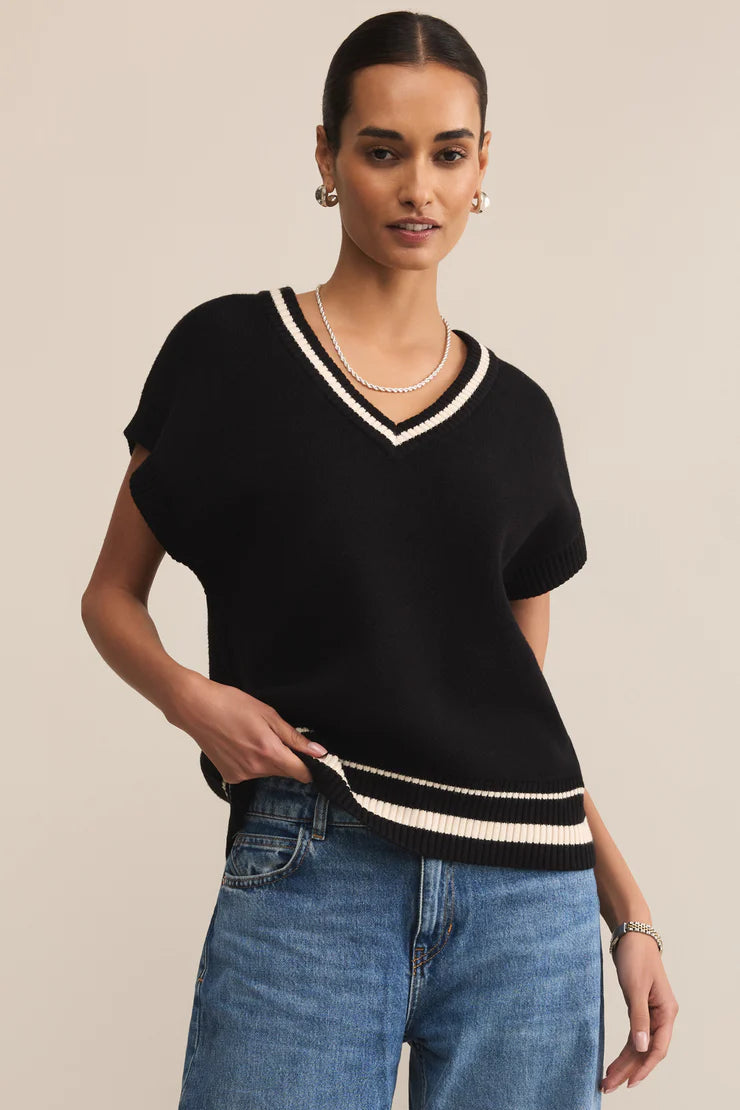Woman wearing a black sweater with white trim and blue jeans on a beige background
