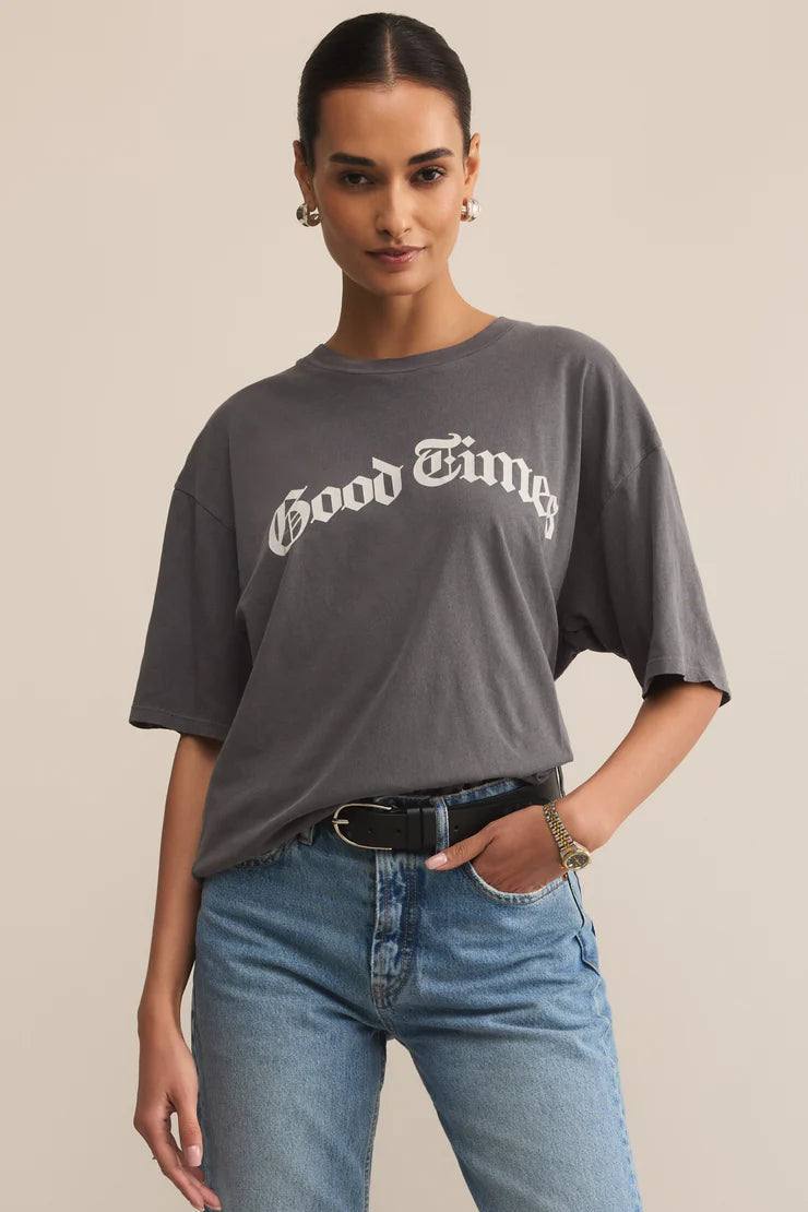Woman wearing a gray 'Good Times' t-shirt and blue jeans on a beige background