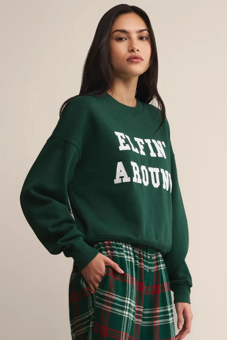 Person wearing a green sweatshirt with 'ELFIN AROUND' text and plaid pants on a beige background