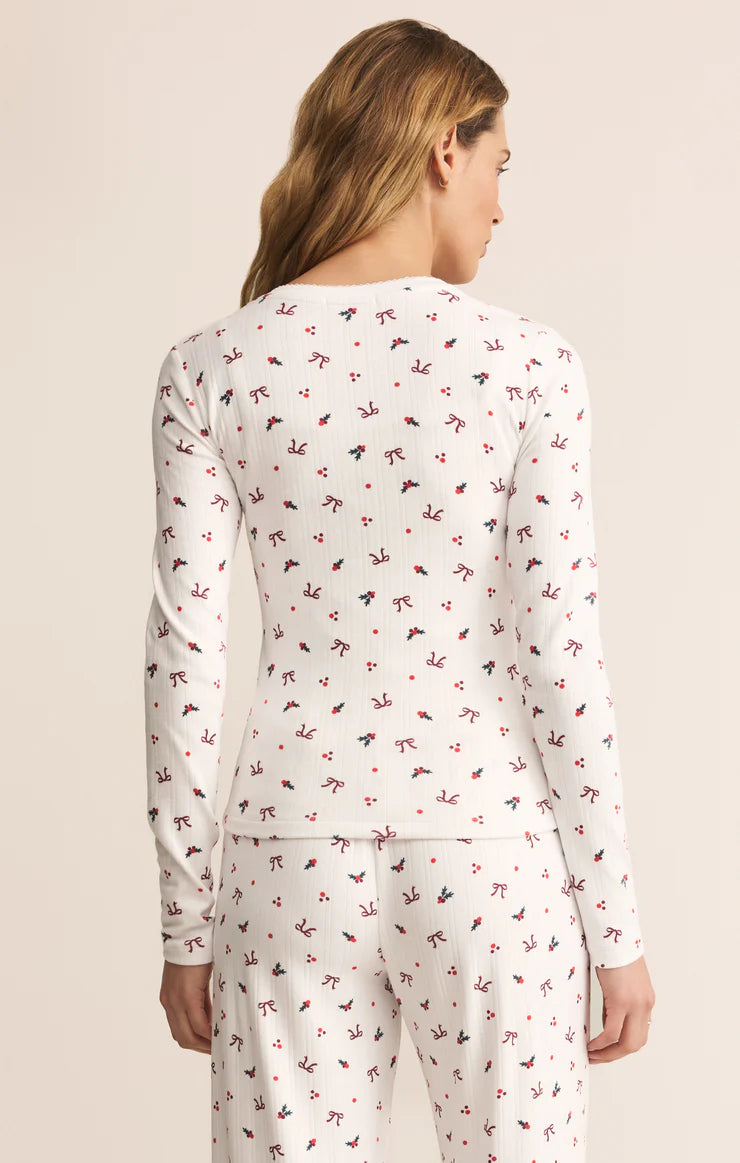 Woman wearing a white Z Supply long-sleeve top with small holiday pattern of bows and holly