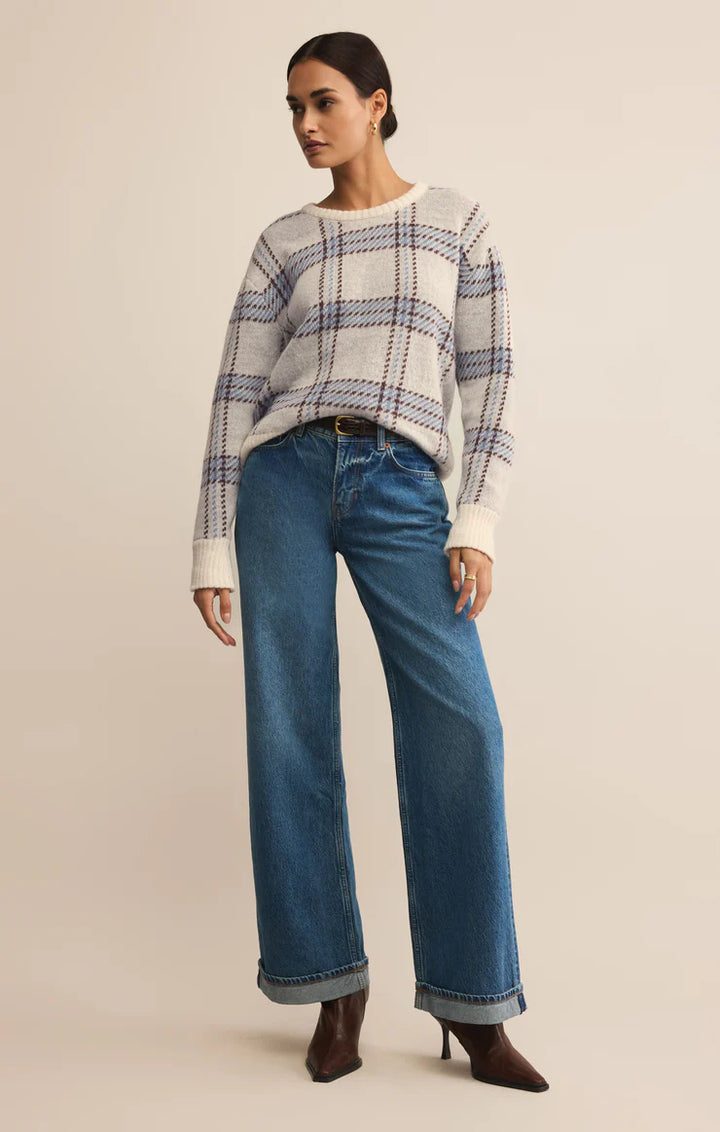Woman wearing a plaid sweater and blue jeans on a beige background