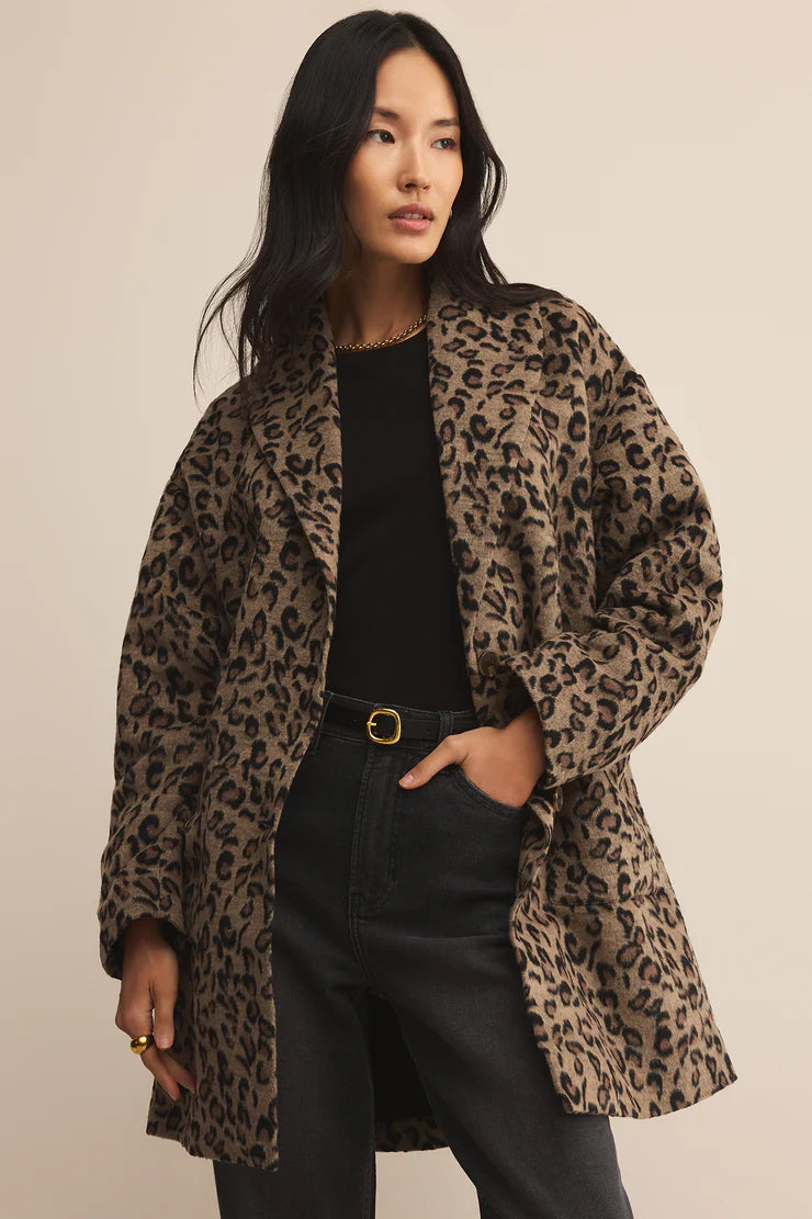 Woman wearing a leopard print coat over a black top and pants on a beige background