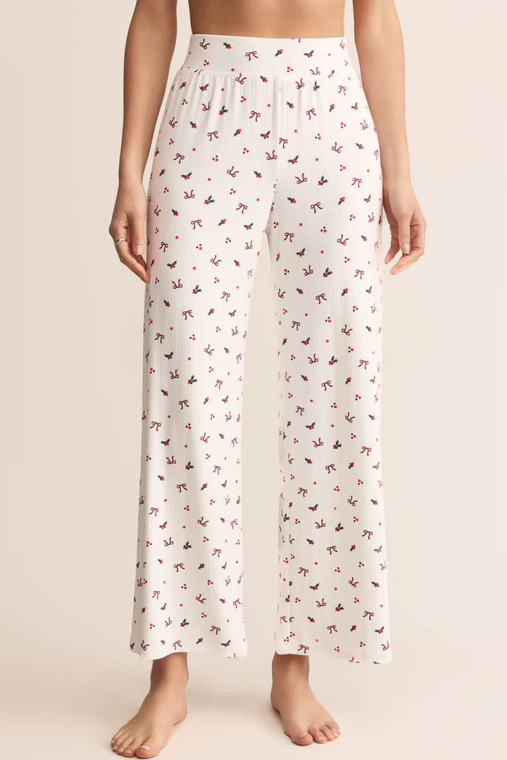 White pajama pants with a subtle bow and holly pattern worn by a person Z Supply