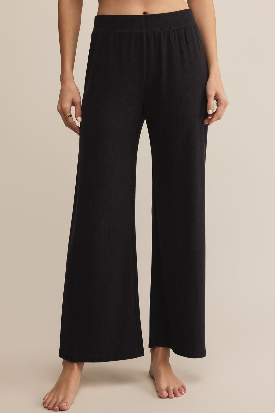 Black wide-leg lounge pants made from pointelle fabric worn by a person on a beige background