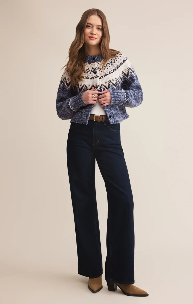 Woman wearing a patterned cardigan and dark jeans on a beige background