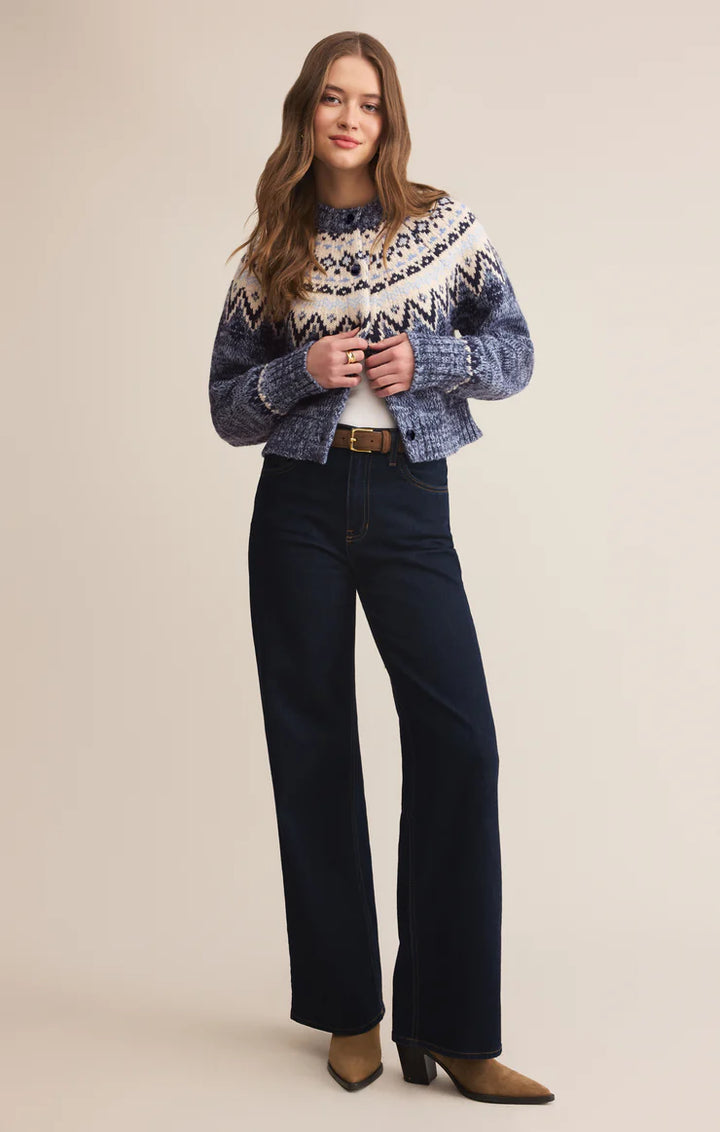 Woman wearing a patterned cardigan and dark jeans on a beige background