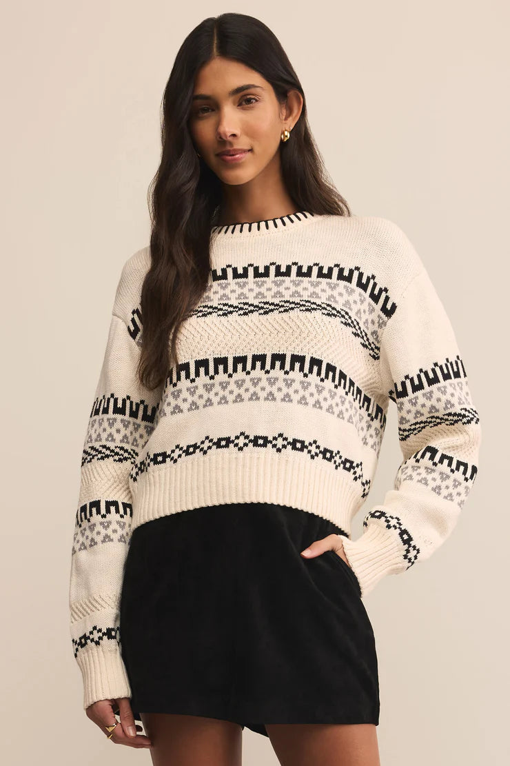Woman wearing a white sweater with black pattern against a beige background