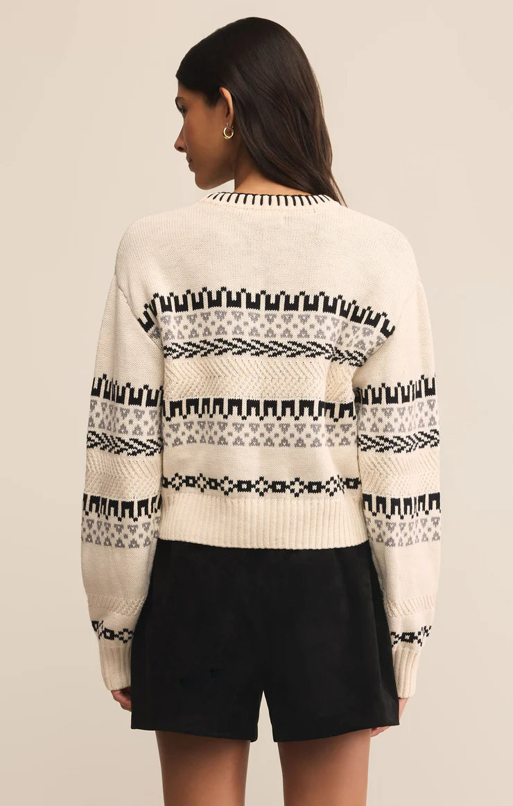 Person wearing a cream sweater with black and white pattern on a beige background