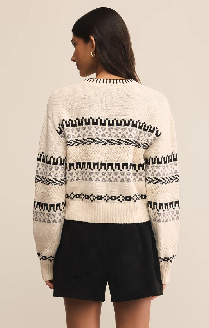 Person wearing a cream sweater with black and white pattern on a beige background