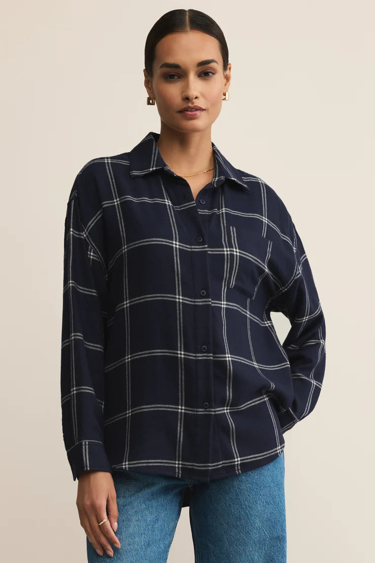 Woman wearing a navy plaid shirt and blue jeans against a beige background