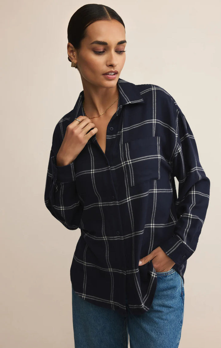 Woman wearing a navy plaid shirt and blue jeans against a beige background