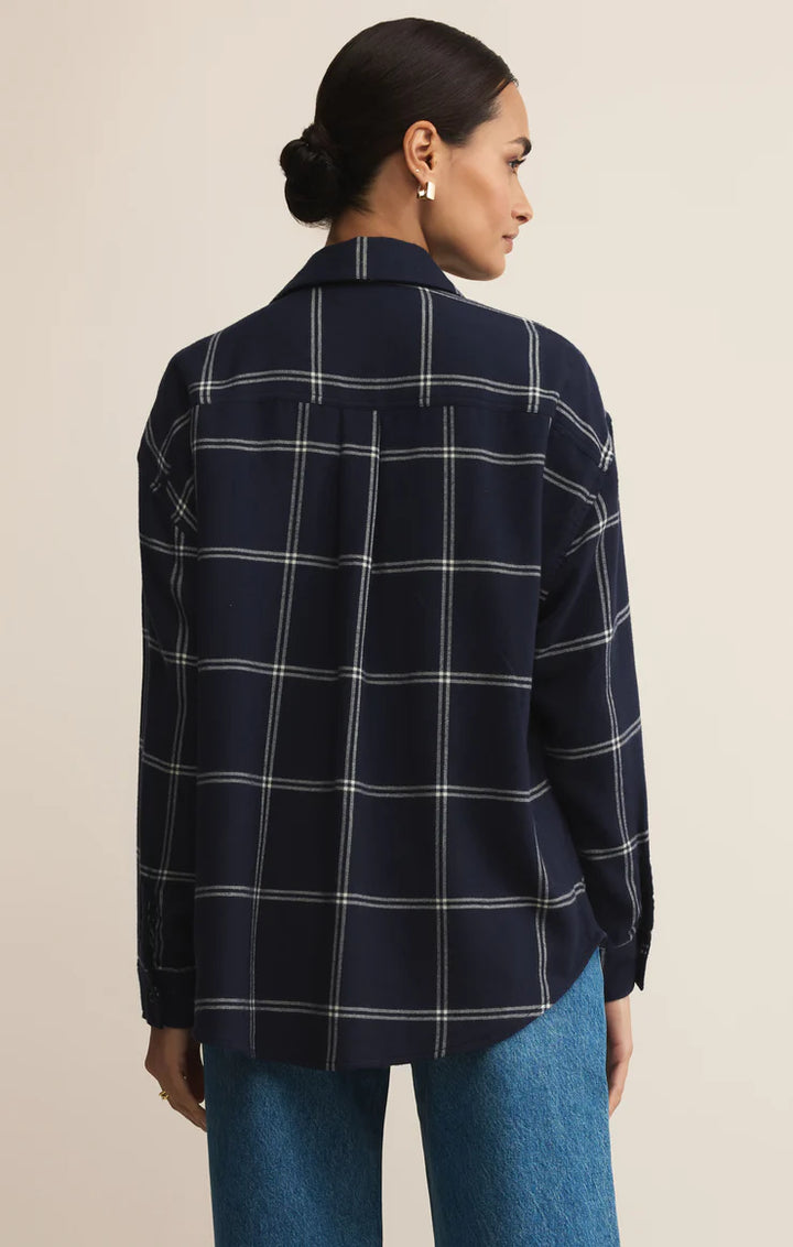 Woman wearing a navy plaid shirt and blue jeans on a beige background