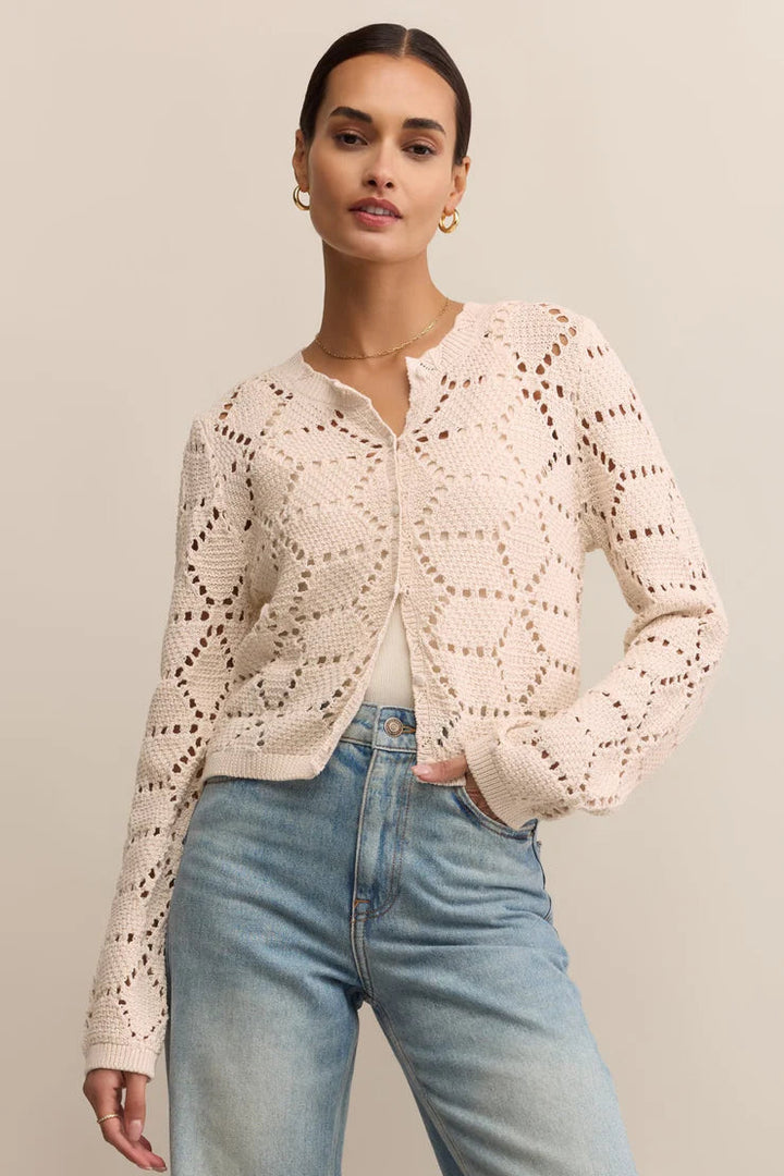 Woman wearing a light pink lace cardigan and blue jeans against a beige background