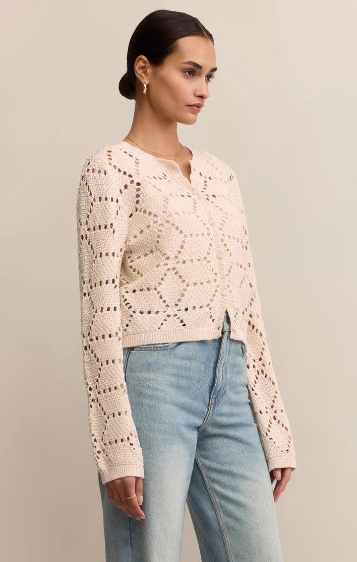 Woman wearing a light pink crochet sweater and light blue jeans against a neutral background