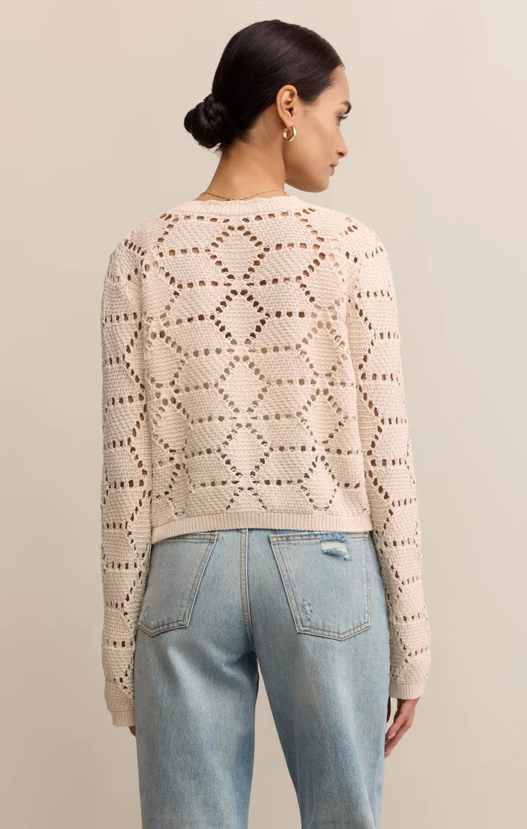 Woman wearing a beige patterned sweater and light blue jeans against a neutral background