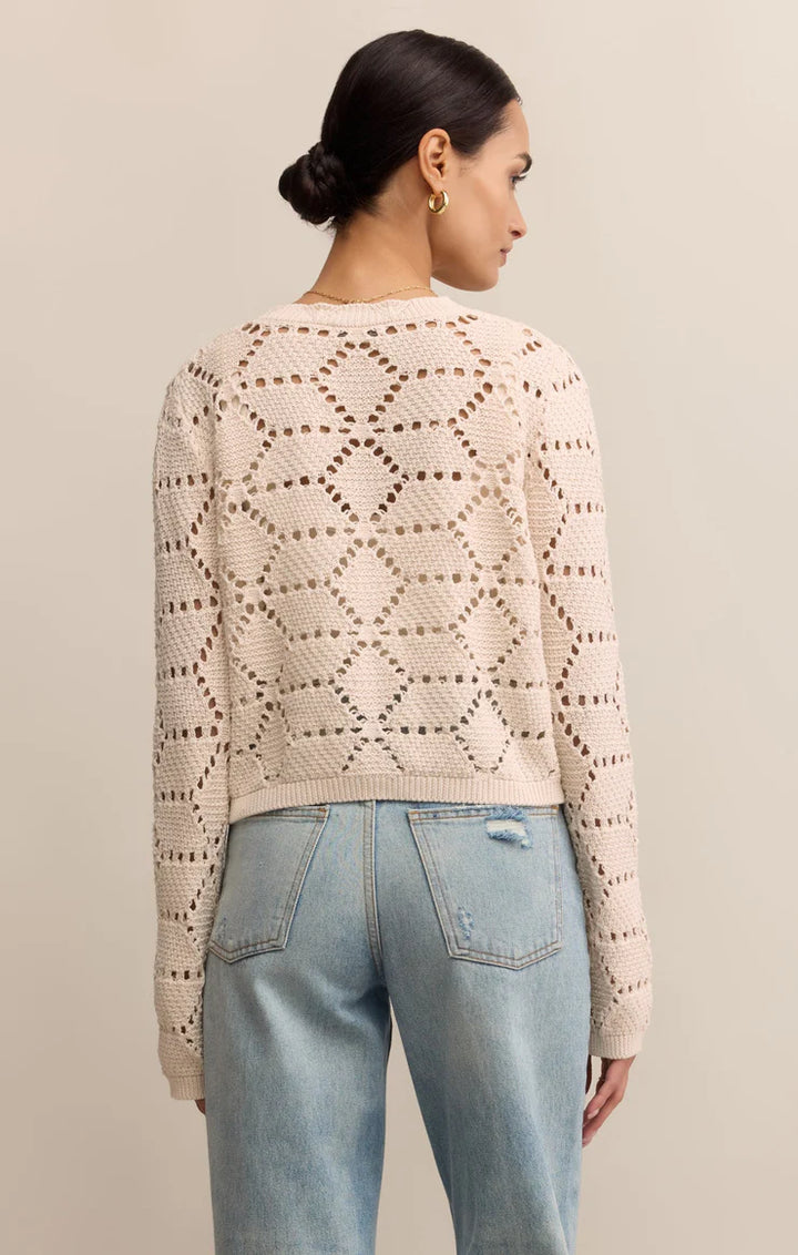 Woman wearing a beige patterned sweater and light blue jeans against a neutral background