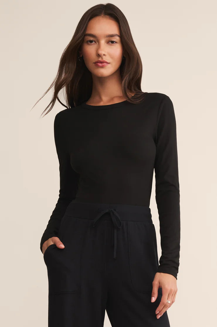 Woman wearing a black long-sleeve top and black pants on a beige background