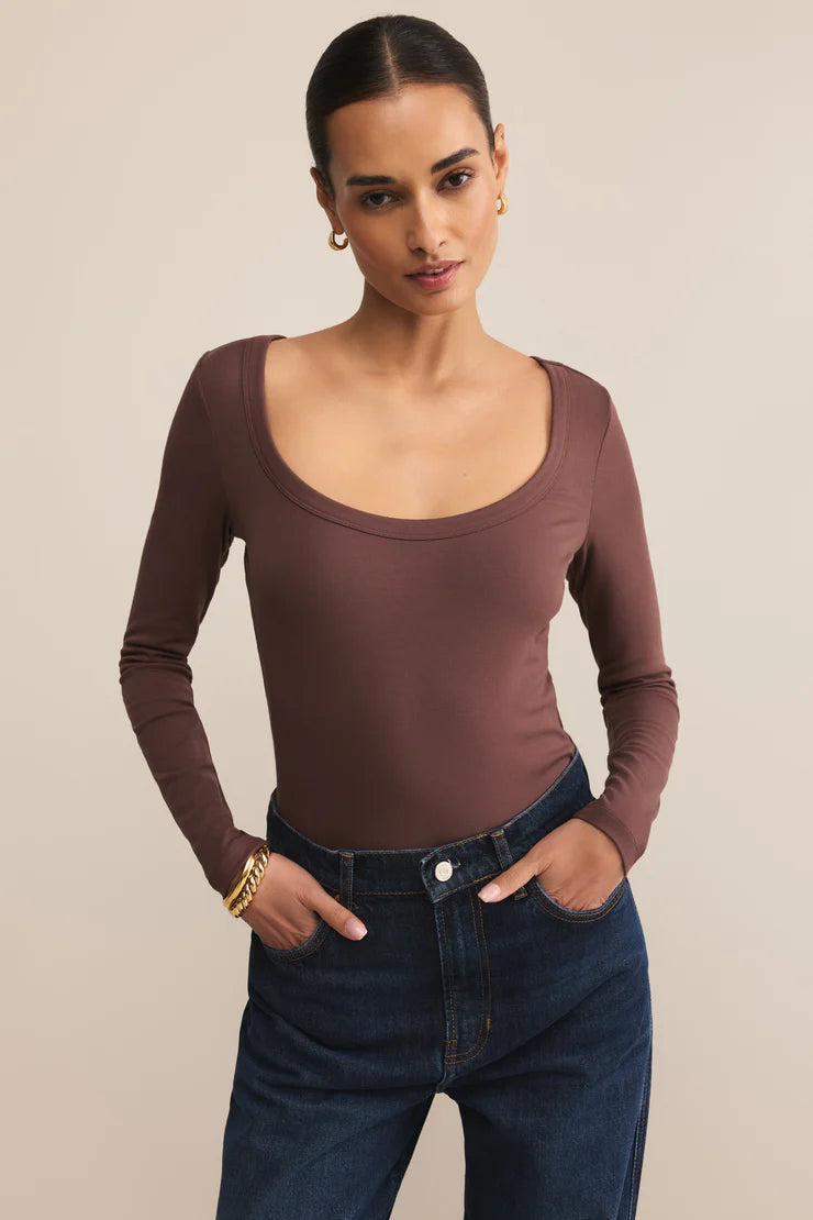 Woman wearing a brown long-sleeve top and blue jeans against a beige background