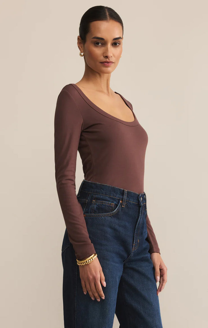 Woman wearing a brown long-sleeve top and blue jeans against a beige background