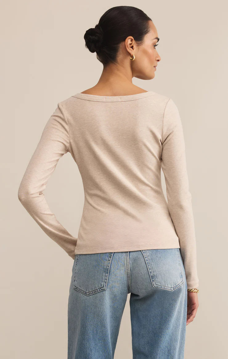 Woman wearing a beige long-sleeve top and blue jeans on a beige background