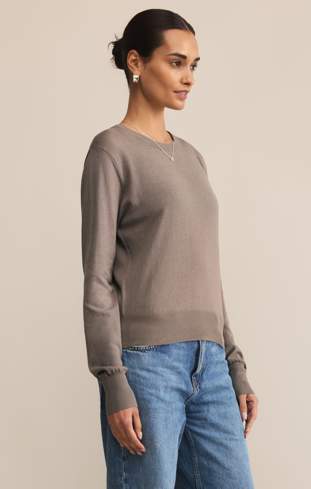 Woman wearing a brown sweater and blue jeans against a beige background