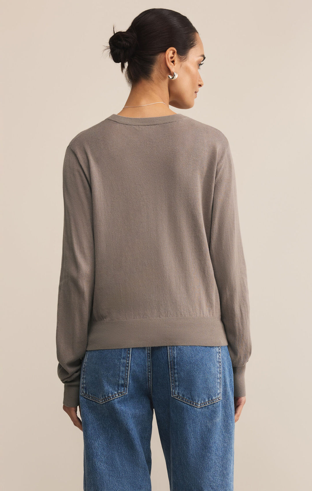 Woman wearing a brown sweater and blue jeans against a beige background