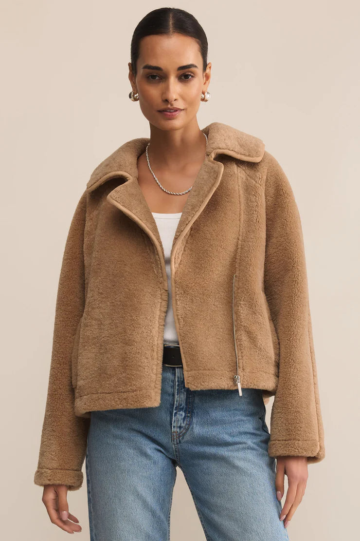 Woman wearing a brown jacket and blue jeans against a beige background