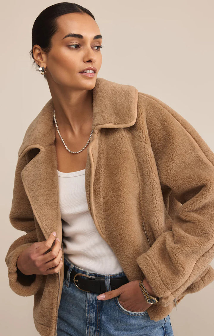 Woman wearing a beige teddy coat over a white top and blue jeans on a beige background