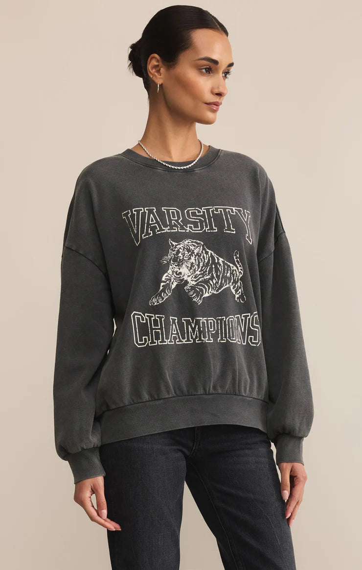 Person wearing a dark gray 'Varsity Champions' sweatshirt with a tiger graphic on a beige background