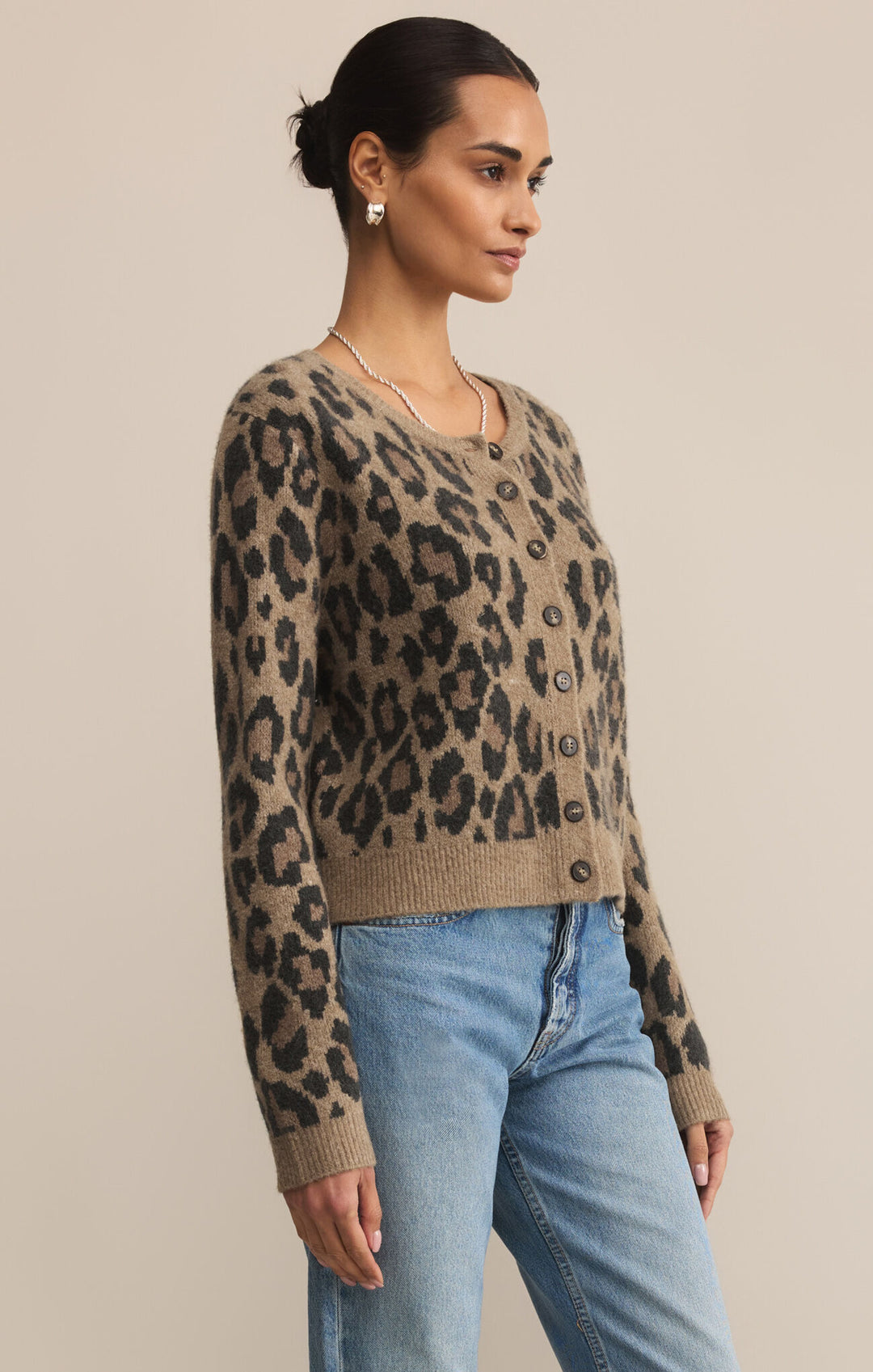 Woman wearing a leopard print sweater and blue jeans against a beige background