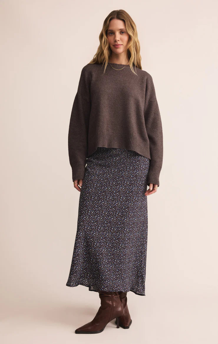 Woman wearing a brown sweater and patterned skirt on a beige background