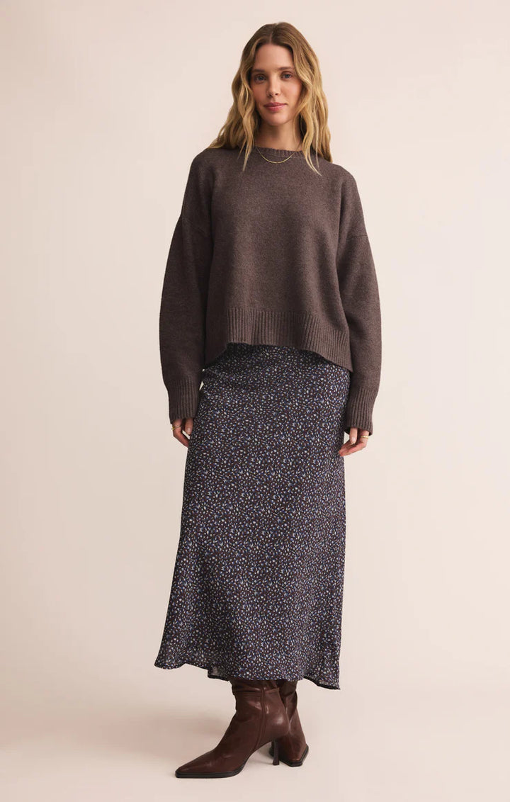 Woman wearing a brown sweater and patterned skirt on a beige background