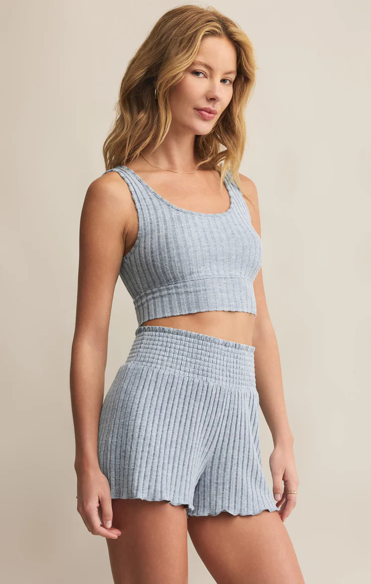 Woman wearing a light blue ribbed crop top and shorts set against a beige background